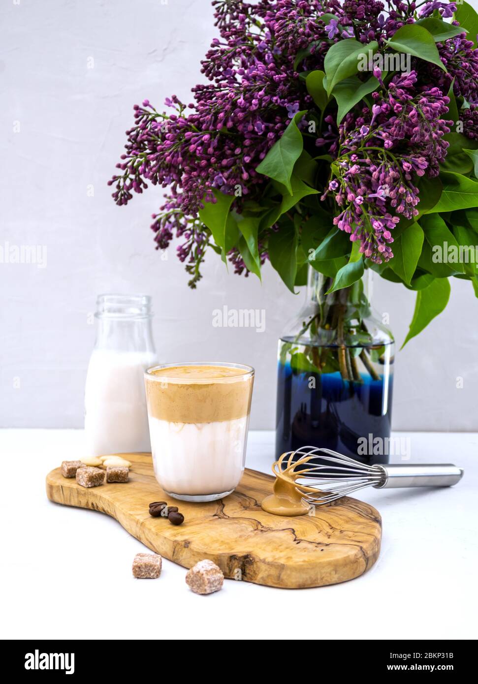 La bevanda coreana Dalgona a base di latte di mandorla con fiore lilla su sfondo bianco Foto Stock