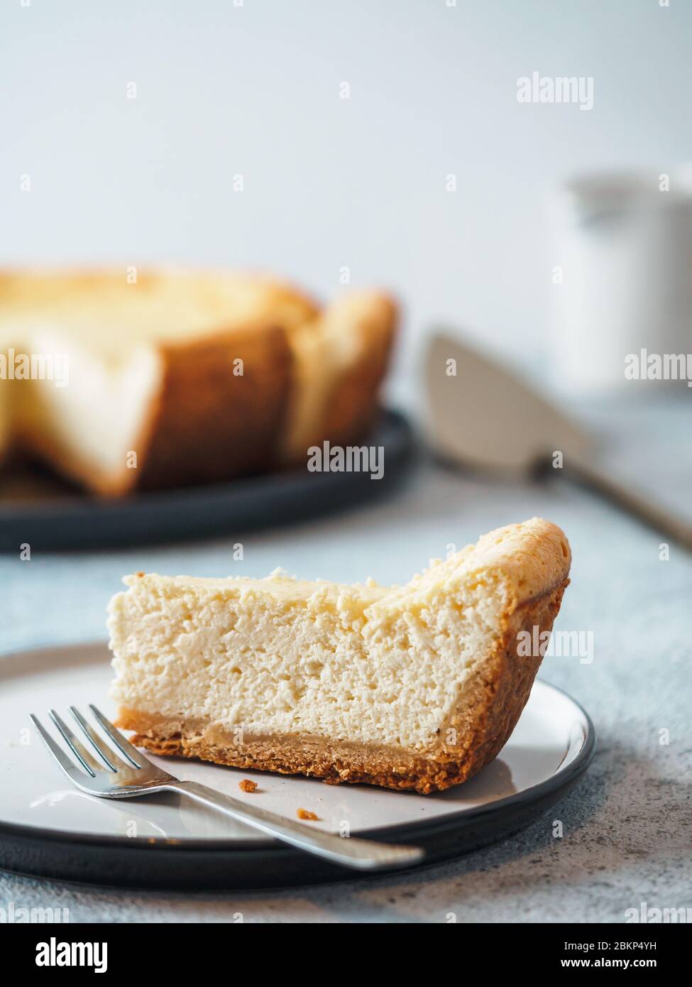 Piatto con pezzo di cheesecake sul piano del tavolo. Cheesecake classico fatto in casa con DOF poco profondo. Verticale. Spazio di copia per il testo. Foto Stock
