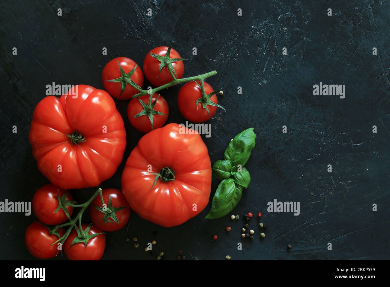 Pomodori freschi su fondo nero con spezie. Vista dall'alto Foto Stock