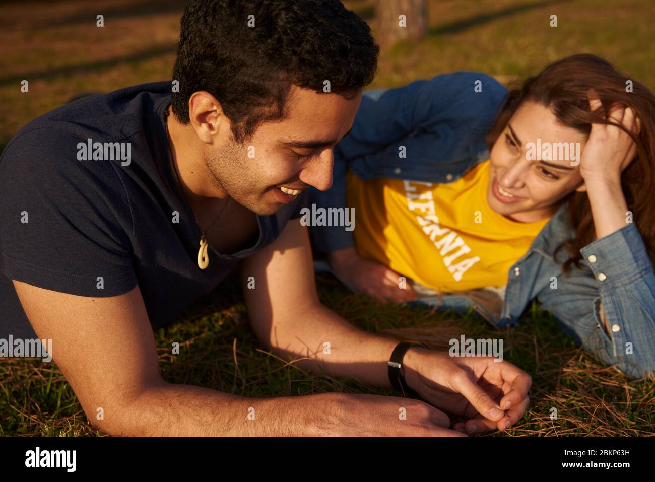 Una coppia adagiata sull'erba in un parco e sorridente l'una all'altra. Foto Stock