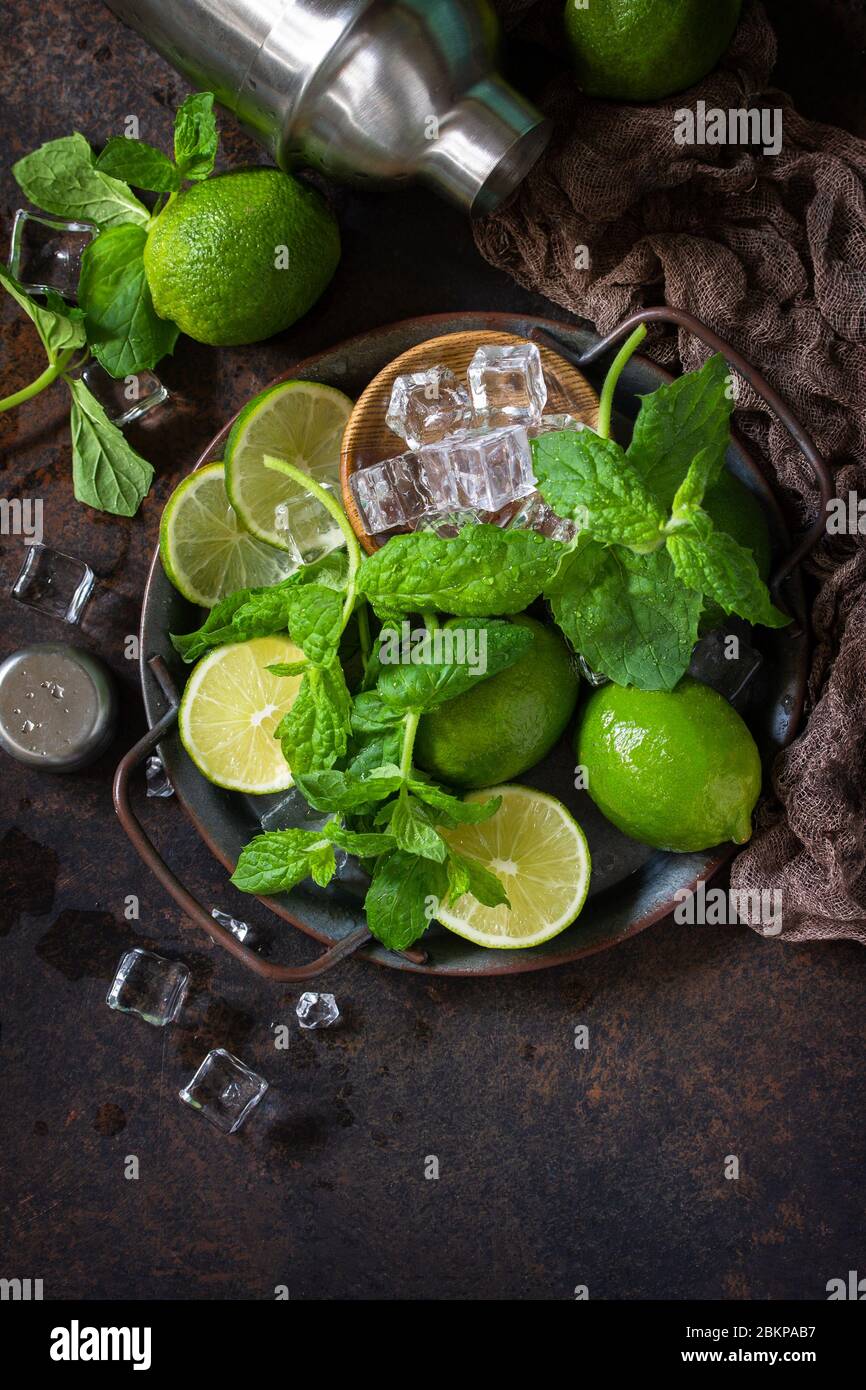 Rinfrescante mojito cocktail making. Ingredienti di menta, calce, ghiaccio e utensili da bar su sfondo di pietra scura. Vista superiore sfondo piatto. Spazio di copia. Foto Stock