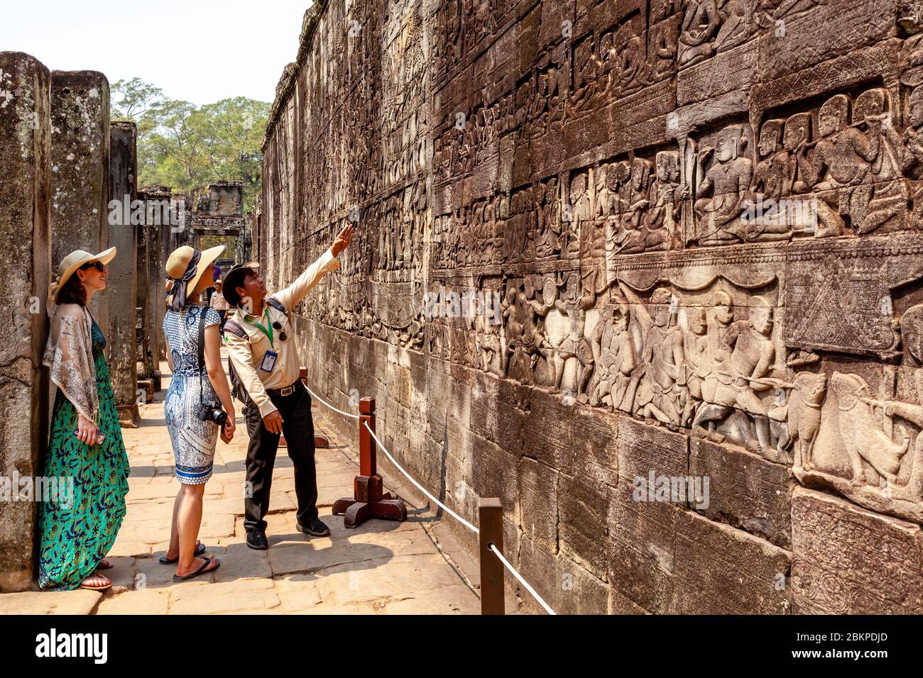 Visitatori femminili che guardano i bassorilievi al Tempio di Bayon, al complesso del Tempio di Angkor Wat, Siem Reap, Cambogia. Foto Stock