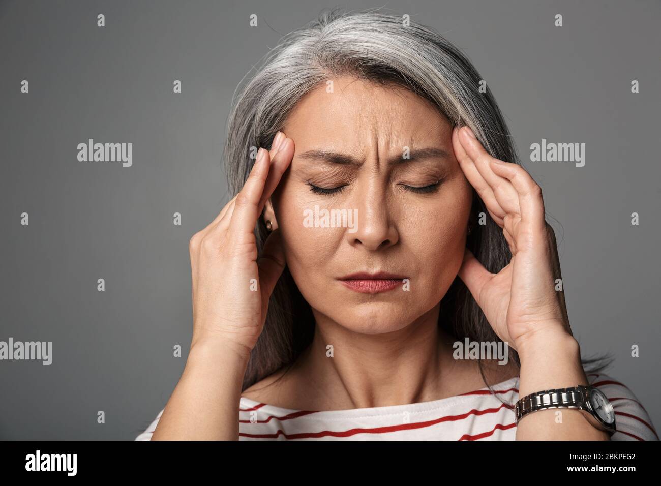 Immagine di donna stanca matura adulto che indossa camicia a righe toccando i suoi templi isolati su sfondo grigio Foto Stock