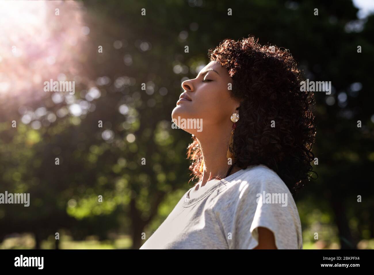 Giovane donna in piedi all'aperto sentire il sole sul suo viso Foto Stock