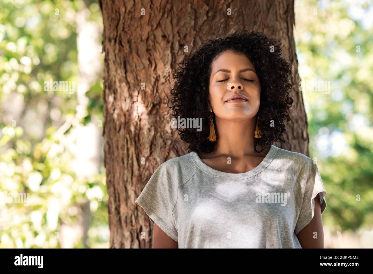 Donna pacifica appoggiata su un albero con gli occhi chiusi Foto Stock