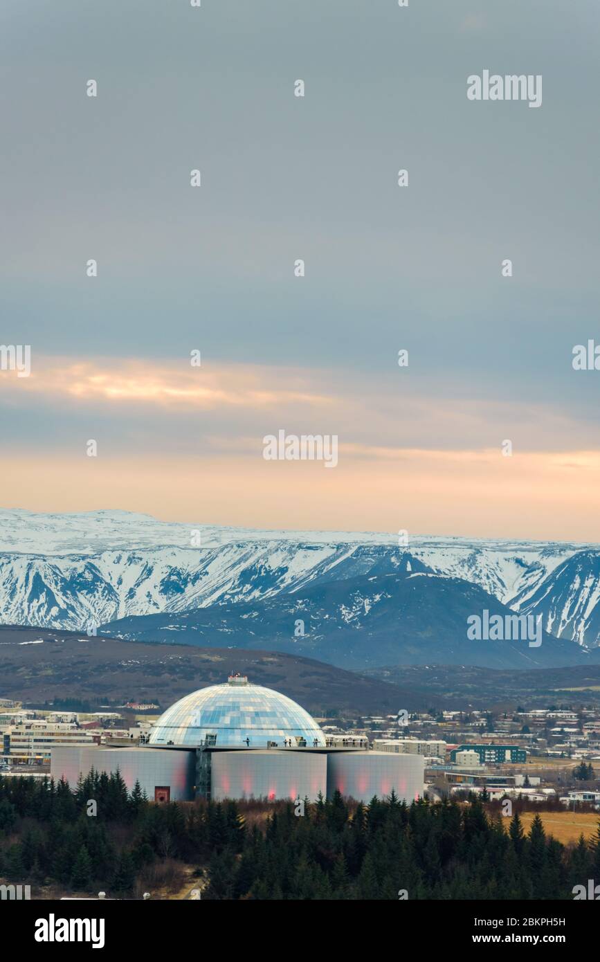 Perlan, edificio simbolo di Reykjavík, la capitale dell'Islanda con montagne innevate sullo sfondo, visto dalla torre della chiesa di Hallgrimskirkja. Foto Stock