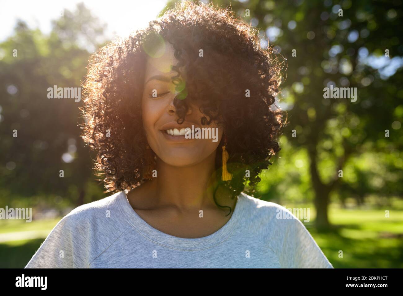 Giovane donna sorridente che si attorciglia i capelli in una giornata di sole Foto Stock