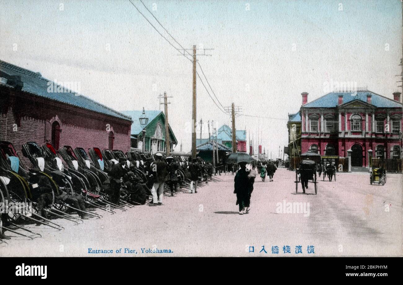 [ 1900 Giappone - ingresso al molo, Yokohama ] - UNA lunga fila di risciò all'ingresso del molo nel porto di Yokohama, Prefettura di Kanagawa. L'edificio in mattoni rossi sulla destra è l'Ufficio del Porto di Kanagawa (神奈川県港務部). Fu progettato dall'architetto britannico Josiah Conder (1852-1920) e completato nel 1890 (Meiji 23). cartolina vintage del xx secolo. Foto Stock