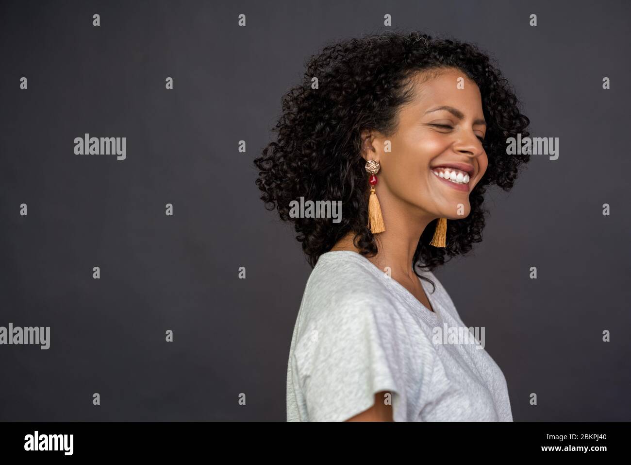 Giovane donna ridente in piedi con gli occhi chiusi su grigio Foto Stock