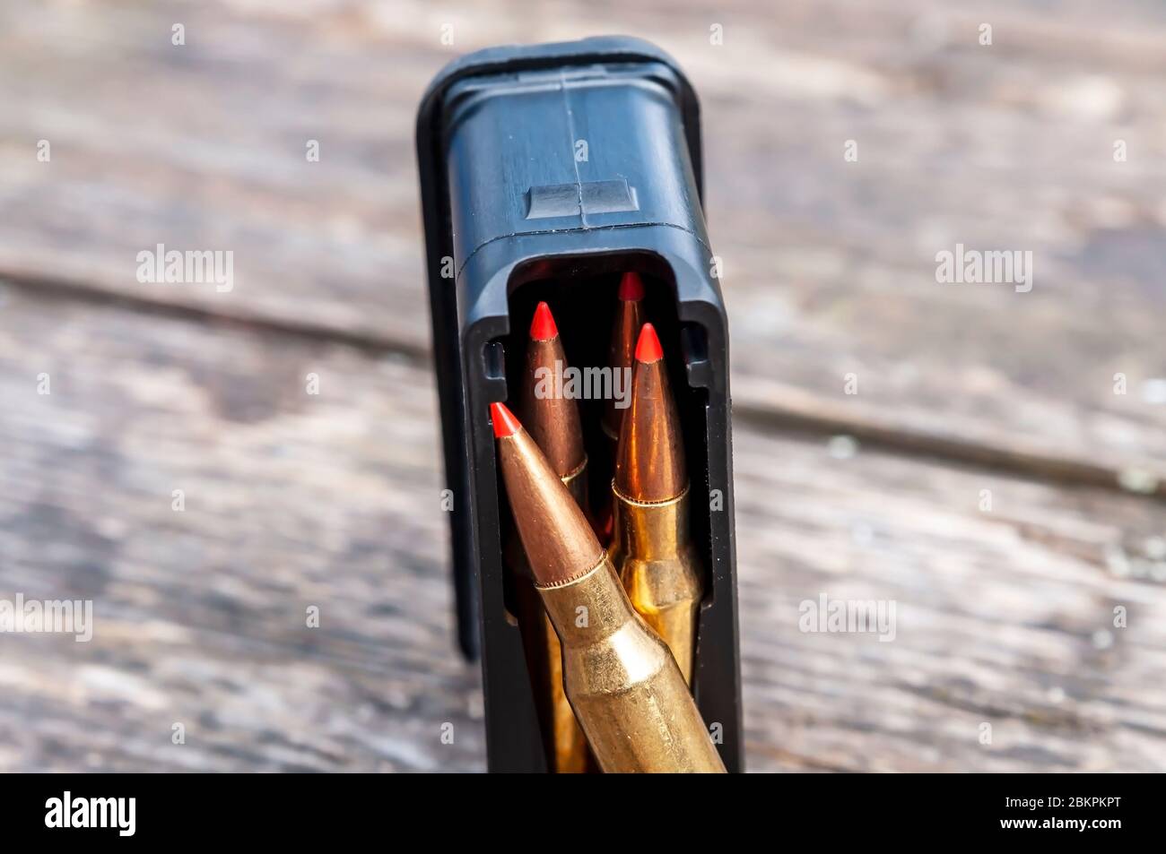 Pallottole rosse in una rivista nera con un fucile appoggiato su uno sfondo di legno Foto Stock