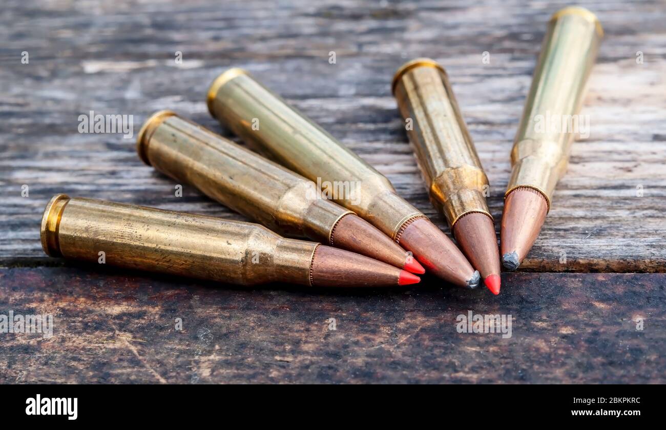 Cinque pallottole di calibro diverso insieme su uno sfondo di legno, tre hanno punte rosse Foto Stock