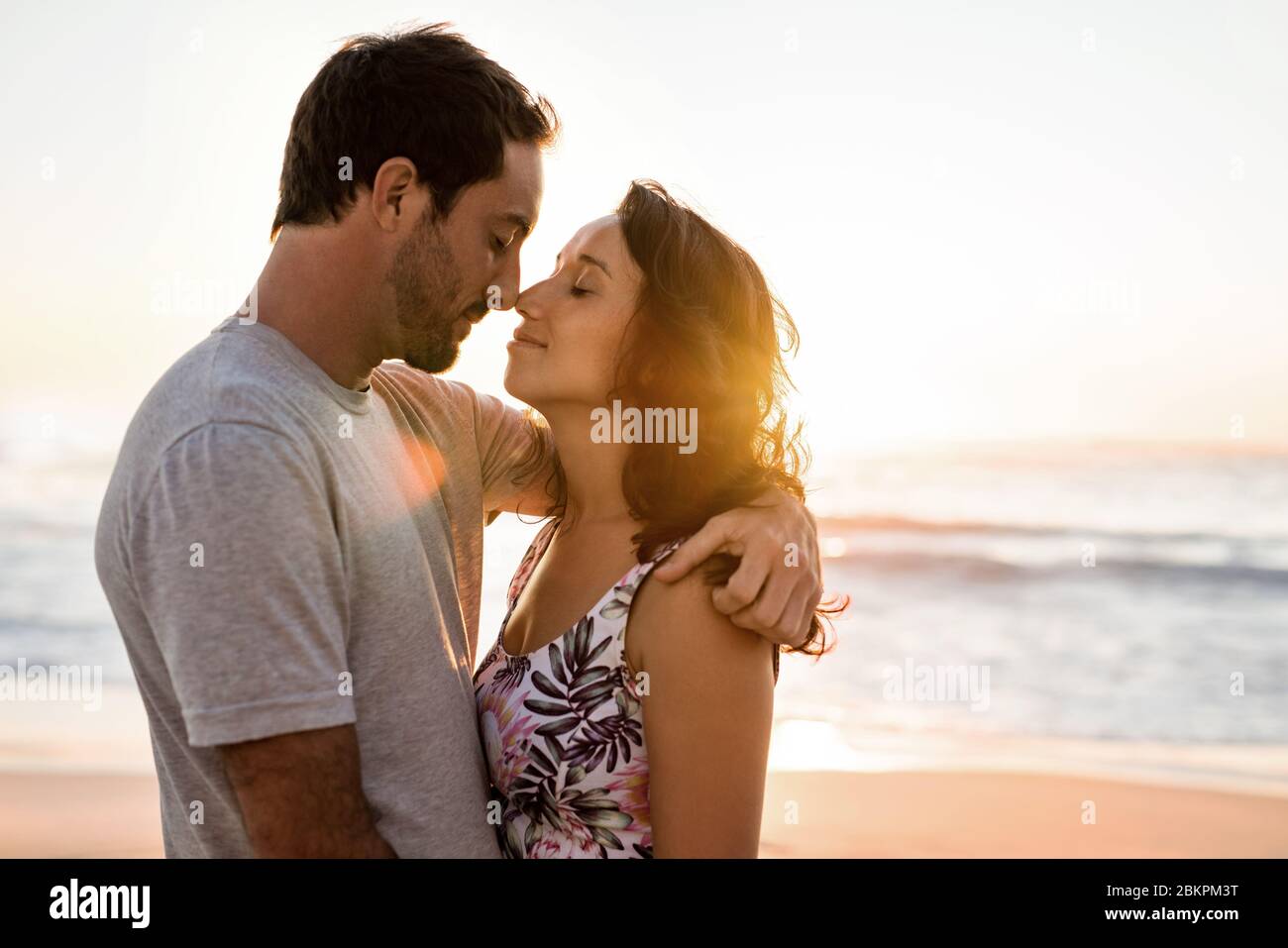 Una giovane coppia che ama abbracciare una spiaggia al tramonto Foto Stock