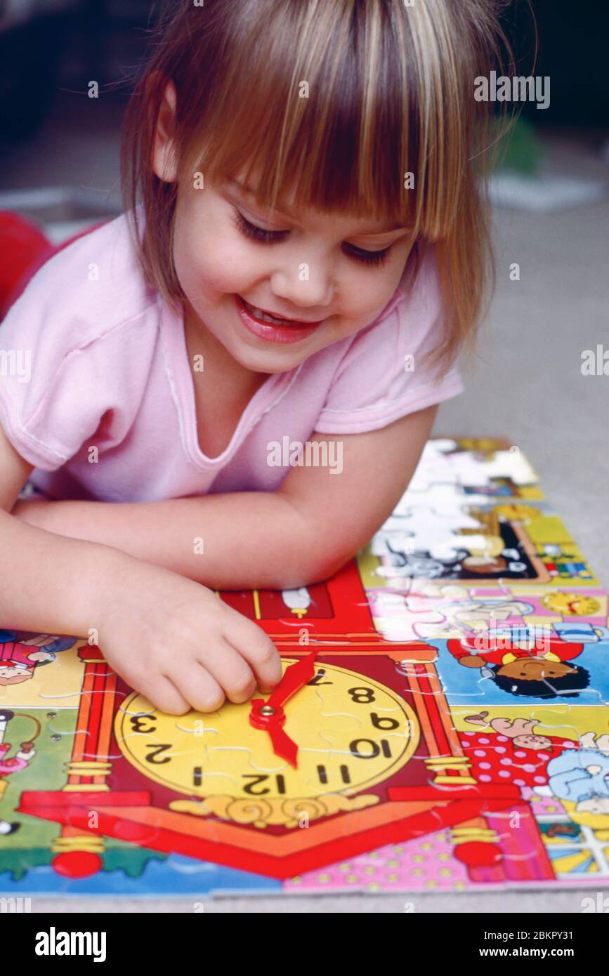 bambino giovane, ragazza, giocando con un puzzle con una foto di un orologio cercando di imparare a raccontare il tempo Foto Stock