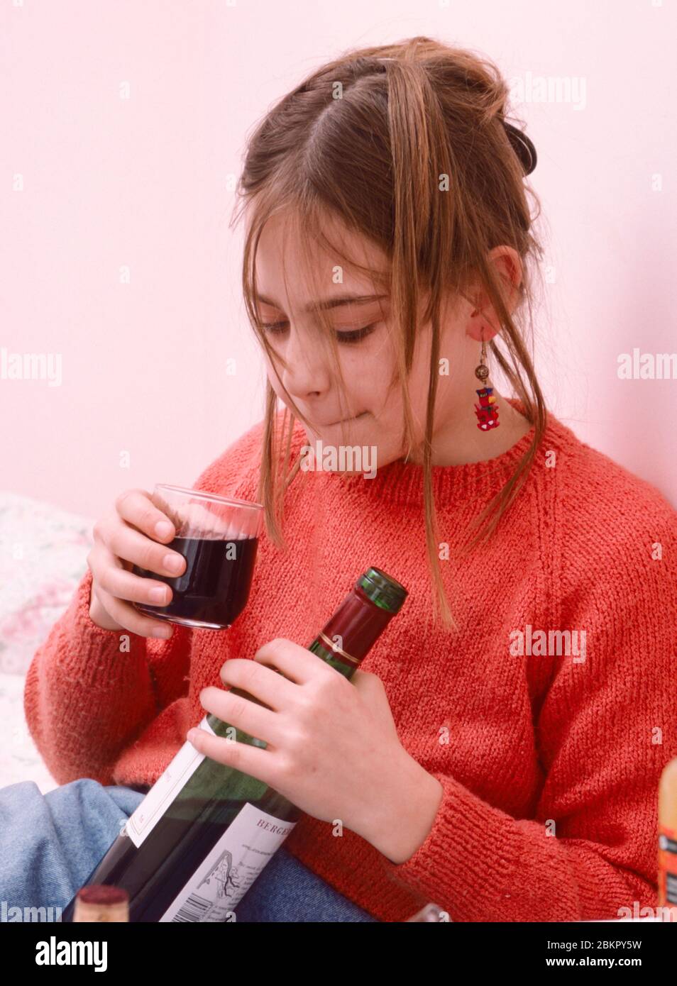 giovane adolescente sperimentando bere vino tenendo bottiglia e bicchiere, bere sotto Foto Stock