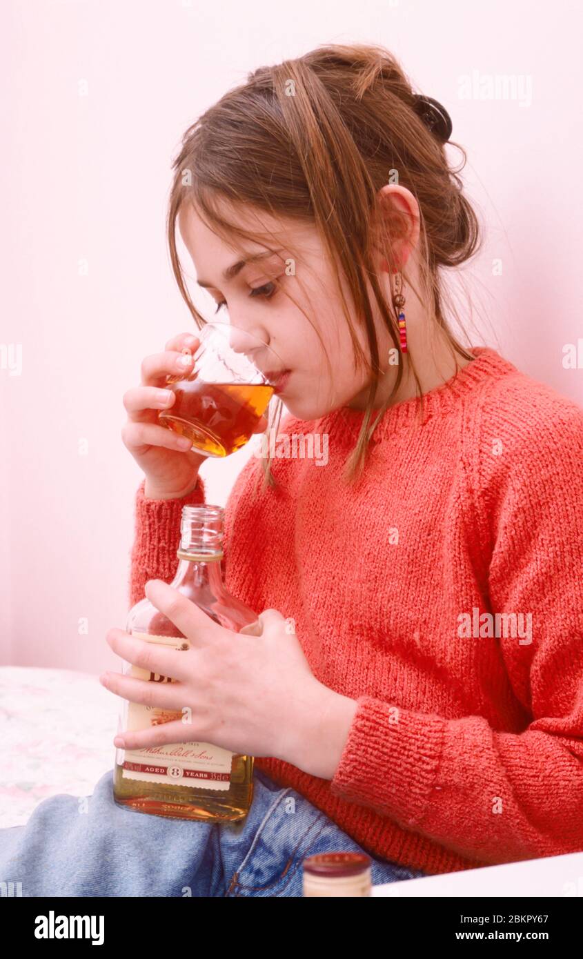 giovane adolescente che sperimenta bevande alcoliche che tengono bottiglia di whisky e vetro, bere sotto Foto Stock