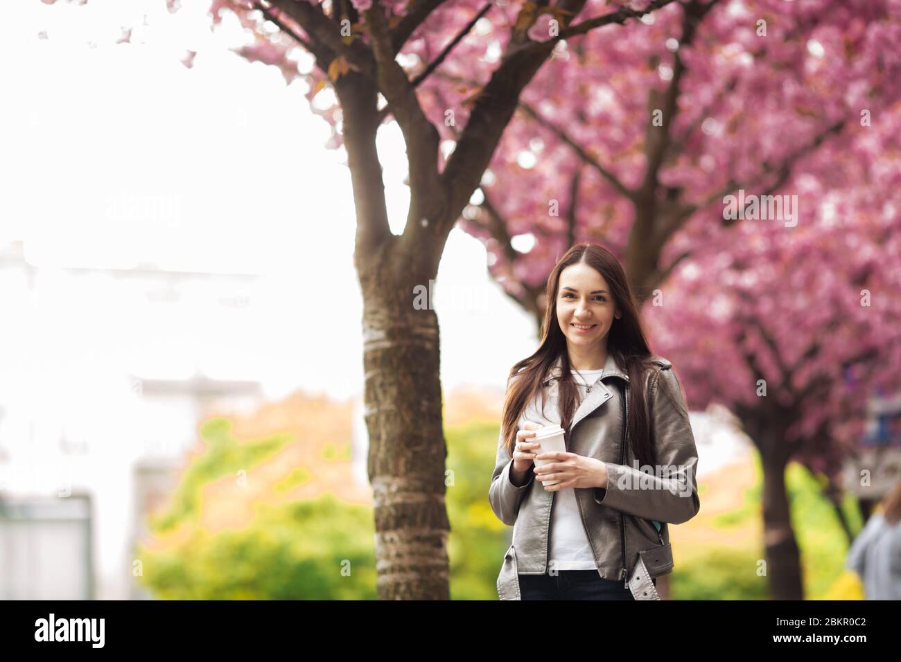 Donna di buon umore che posa con una tazza di caffè contro l'albero di sakura. Foto Stock