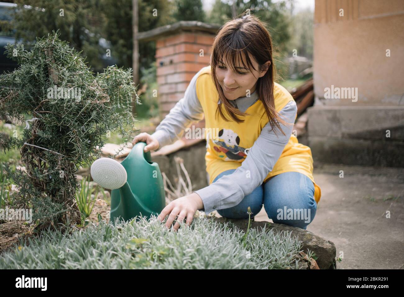 Giovane donna che cura piante mentre li innaffia. La signora che tocca i  fiori mentre tiene annaffiatura può in cortile Foto stock - Alamy