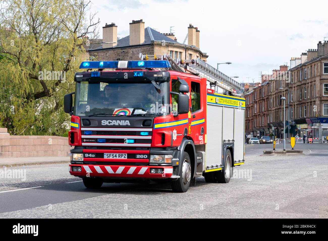 Motore antincendio con luci blu che rispondono a un'emergenza durante il blocco dei coronavirus, Glasgow, Scozia, Regno Unito - con immagine dell'arcobaleno sul parabrezza Foto Stock
