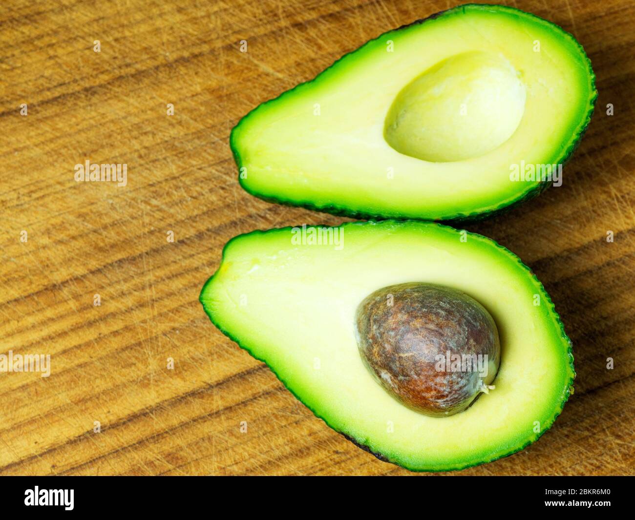 Un avocado dimezzato con la pietra in una metà su un tagliere in legno Foto Stock