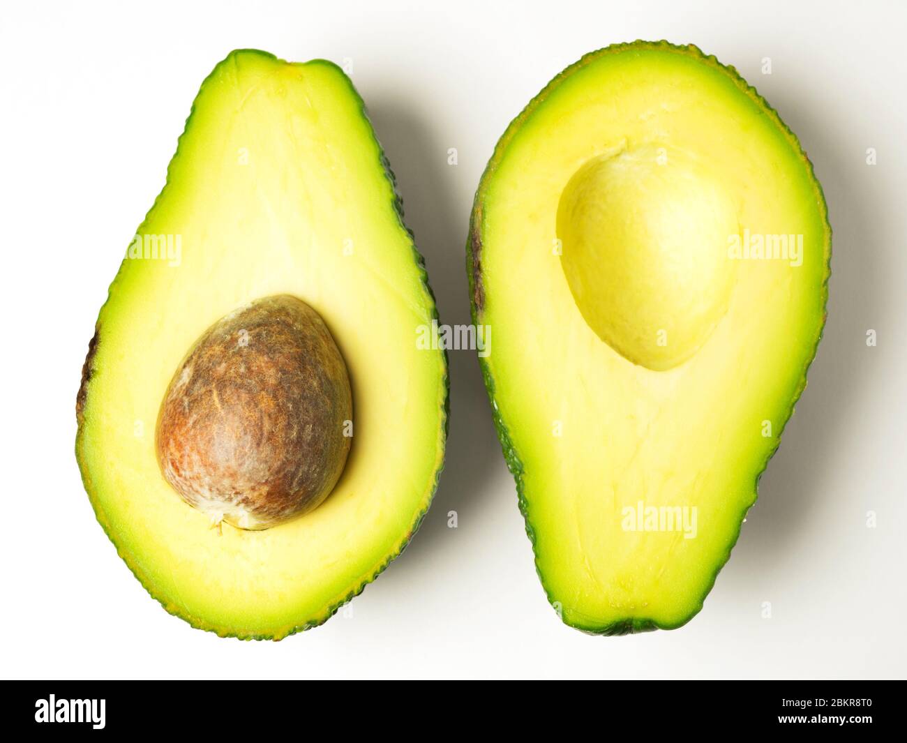 Due metà di avocado opposte verso l'alto con la pietra a sinistra in una metà su uno sfondo bianco Foto Stock