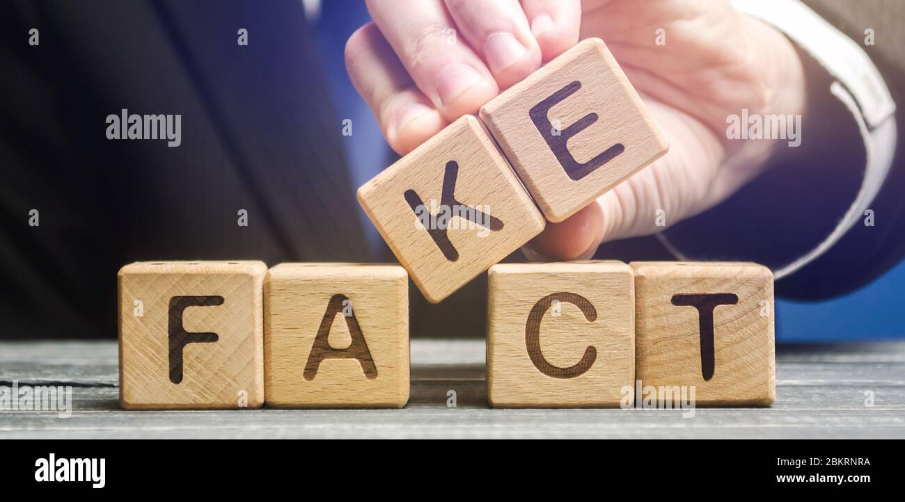 Un uomo mette blocchi di legno con le parole fatto e falso. Concetto di notizie e informazioni false. Premere giallo. Foto Stock