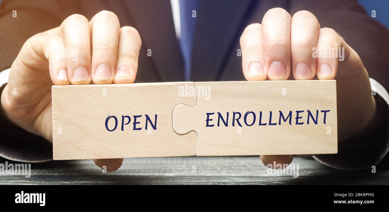 Businessman raccoglie puzzle di legno con parole Open Enrollment. Periodo annuale di inizio dell'assicurazione negli Stati Uniti. Assicurazione sanitaria, medicare. Foto Stock