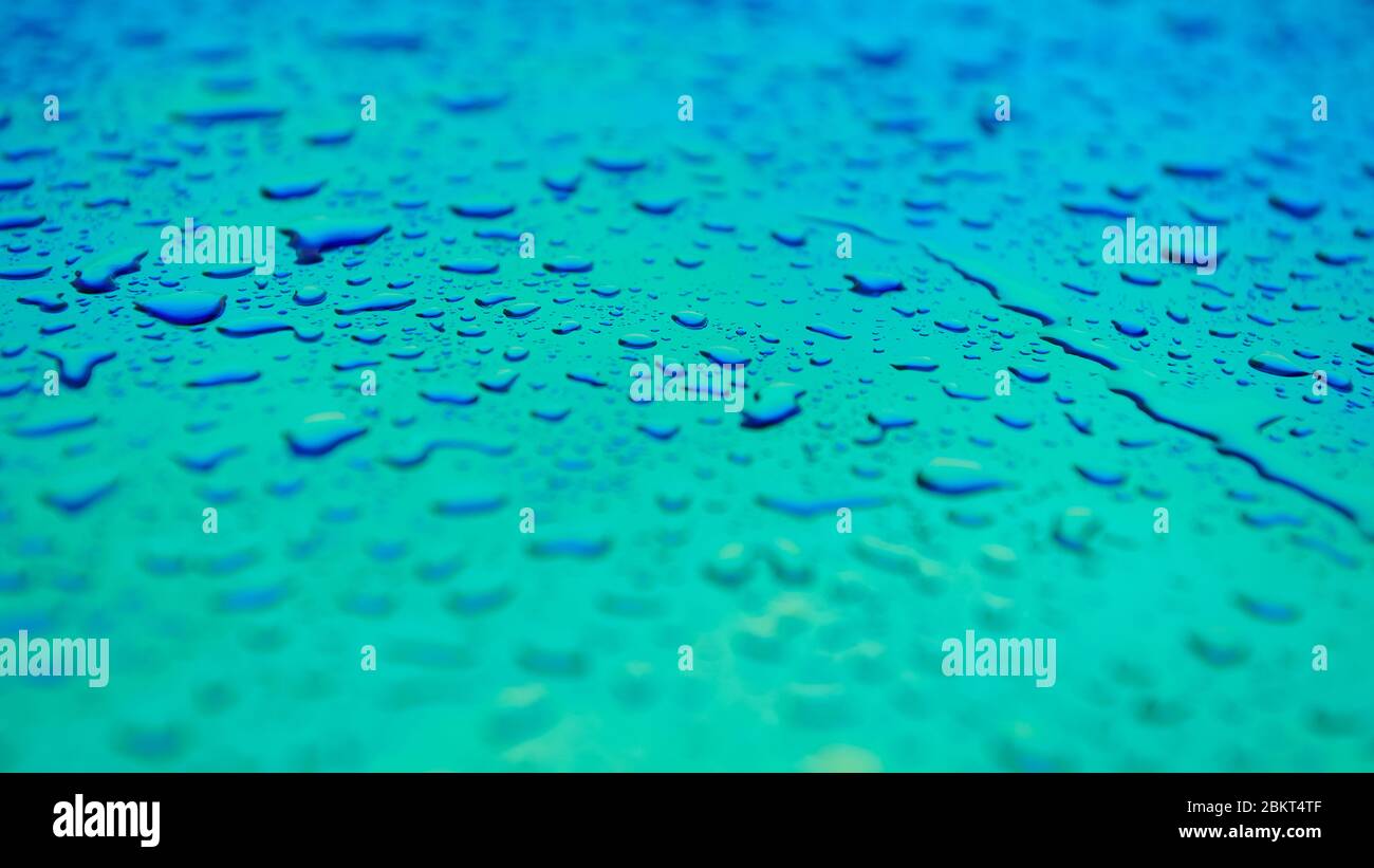 Gocce d'acqua sulla superficie blu e acquamarina. Splendido sfondo colorato con profondità di campo poco profonda. Foto di concetto di freschezza. Formato Web esteso. Foto Stock