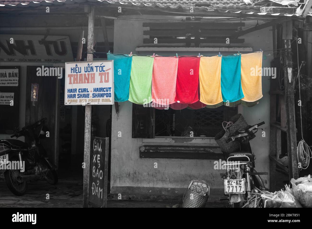 Hoi An Vietnam Ottobre 19 2013; fila di asciugamani colorati che asciugano accanto al parrucchiere segno in entrambi vietnamita e inglese all'aperto in strada in bianco e nero Foto Stock