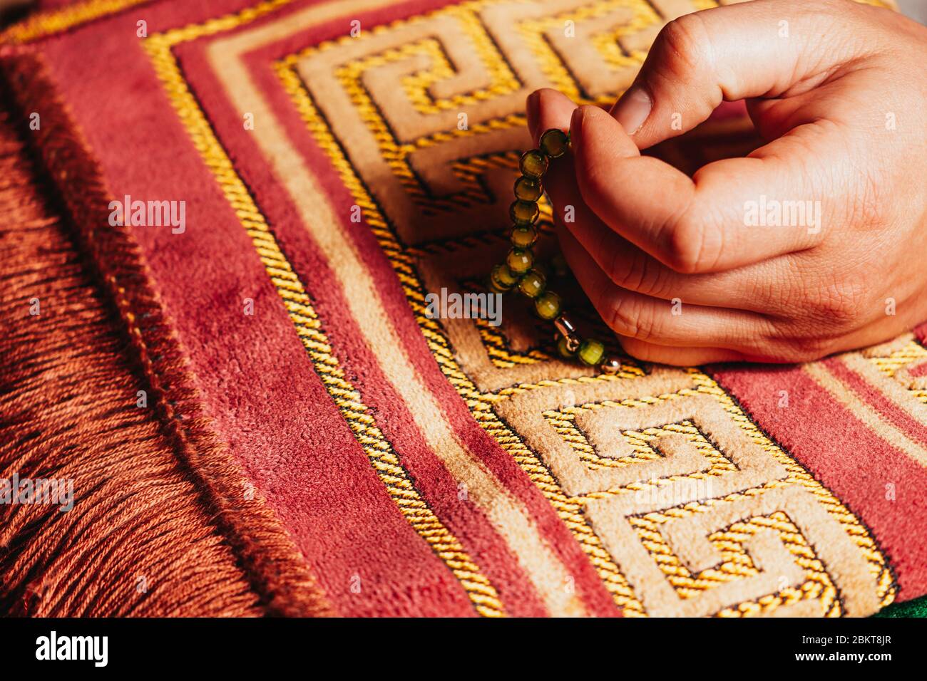 Tenere in mano la preghiera musulmana perla tasbih per la preghiera sul tappeto a Ramadan Kareem Foto Stock