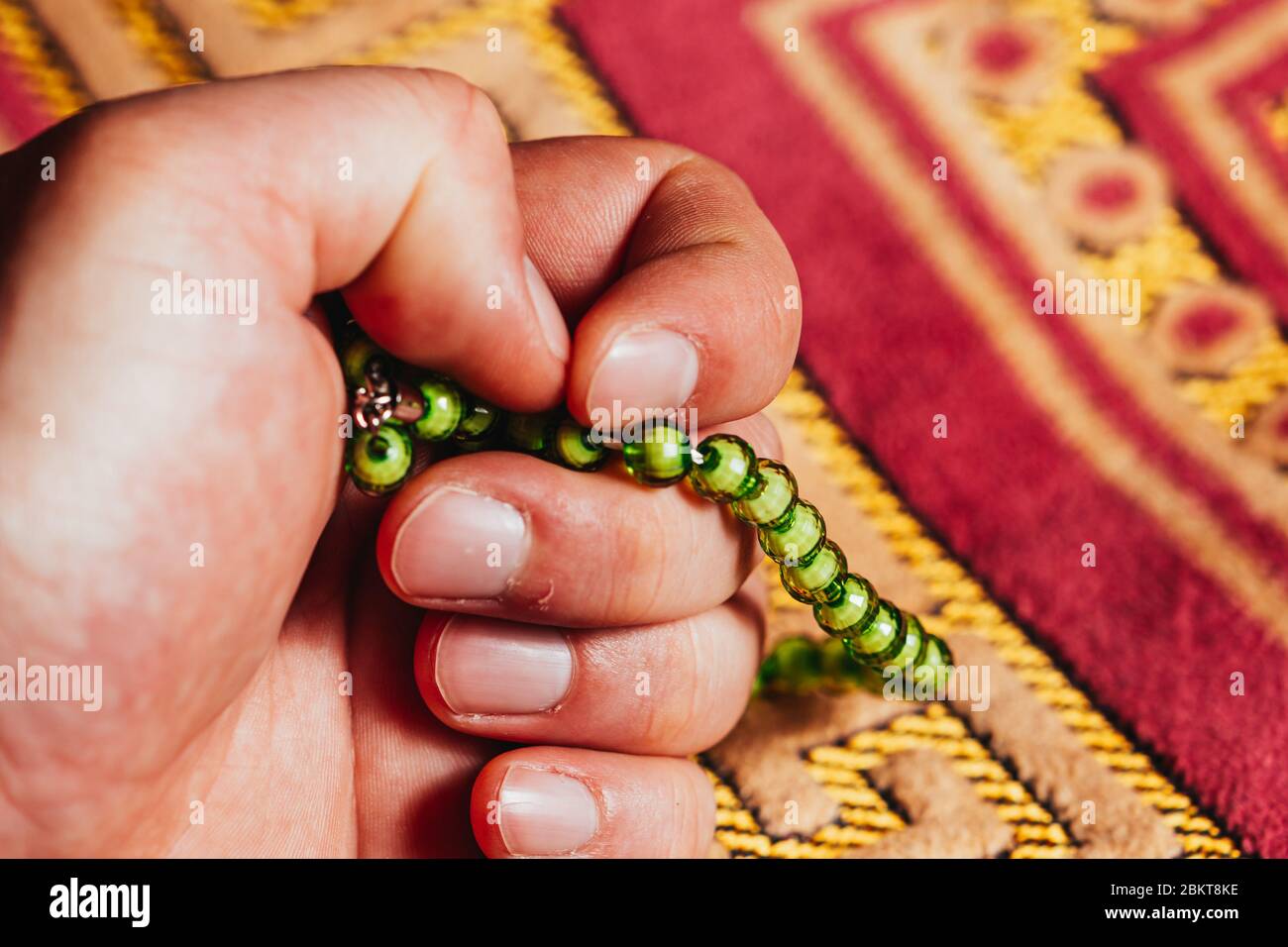 Tenere in mano la preghiera musulmana perla tasbih per la preghiera sul tappeto a Ramadan Kareem Foto Stock