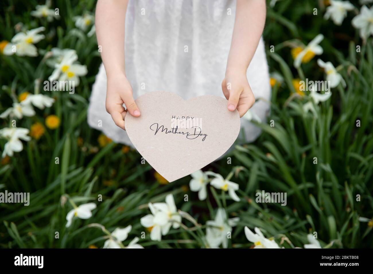 Felice Festa della mamma scritto su una carta tenuta da una ragazza su un fiore e sfondo d'erba Foto Stock