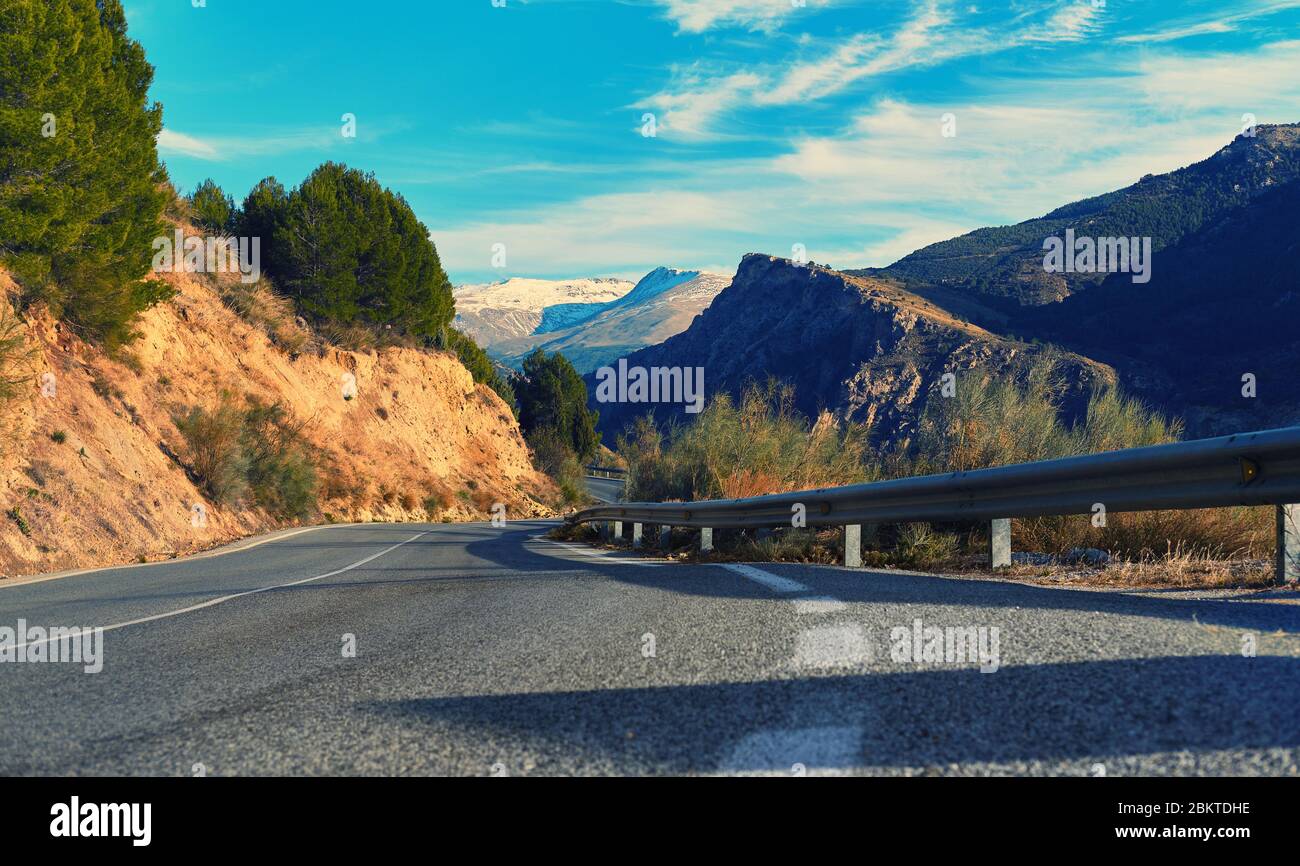 Pittoresca strada di campagna vuota e tortuosa che conduce alla Sierra Nevada innevata cresta. Foto scattata a Granada città spagnola, stazione sciistica. Giorno di sole Foto Stock