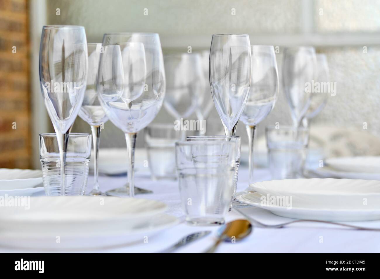 Primo piano nuovo vario di vetreria e piatti di porcellana serviti su tovaglia bianca, non persone. Le impostazioni del tavolo attendono gli ospiti a casa o al ristorante Foto Stock