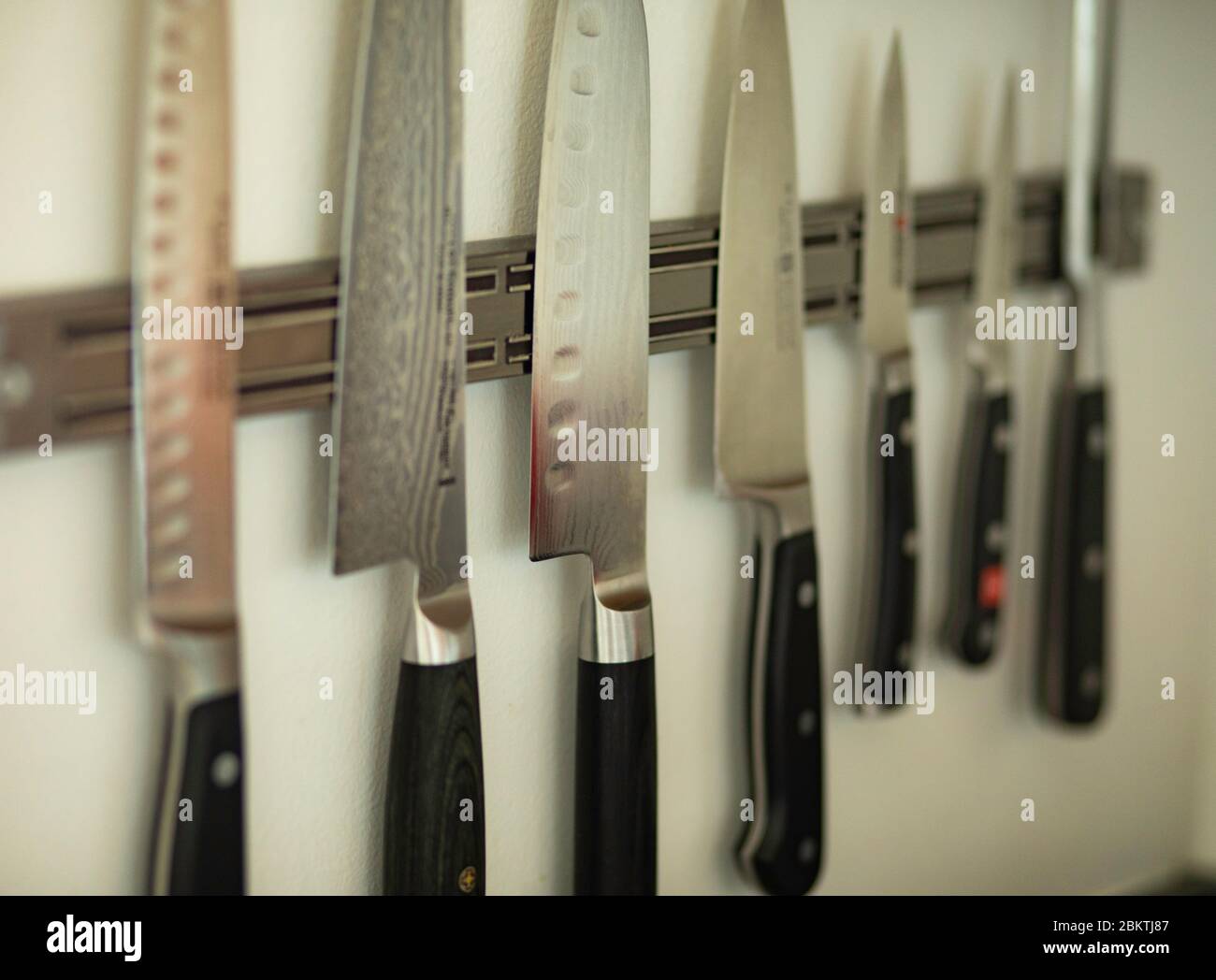 Coltelli professionali dello Chef appesi su una rastrelliera magnetica su una parete bianca Foto Stock