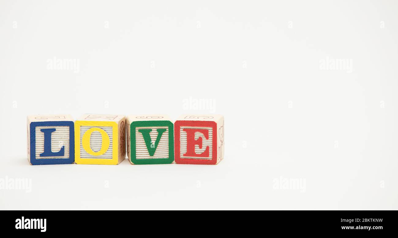 Piccoli blocchi di giocattoli in legno spiegano la parola amore in lettere colorate su uno sfondo bianco. Foto Stock