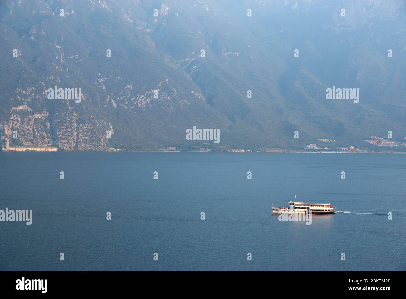 Traghetto per piccoli passeggeri che trasporta turisti sul lago di Garda, nord italia. Serata silenziosa 2019 settembre. Acqua dolce e montagne sullo sfondo. Foto Stock