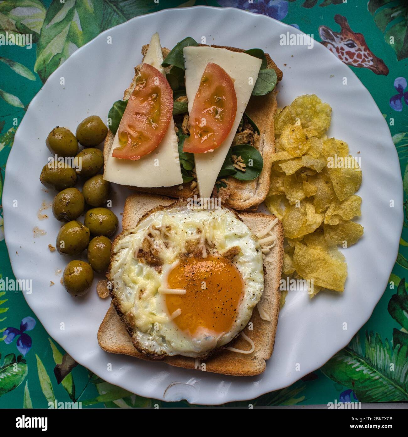 Un piatto con uova fritte con formaggio e pepe su pane affettato, pomodoro, formaggio, patatine, olive e verdure Foto Stock