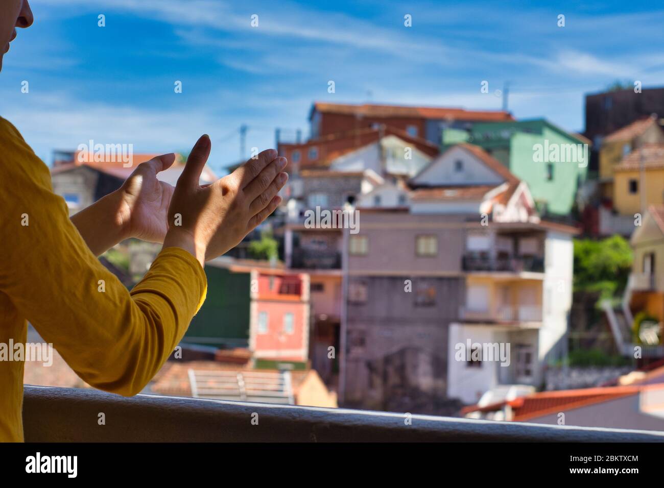 Giovane donna che le ha aggrappato le mani sul balcone per showi gratitudine a tutti gli operatori sanitari durante l'epidemia di coronavirus. Molte case colorate. Foto Stock