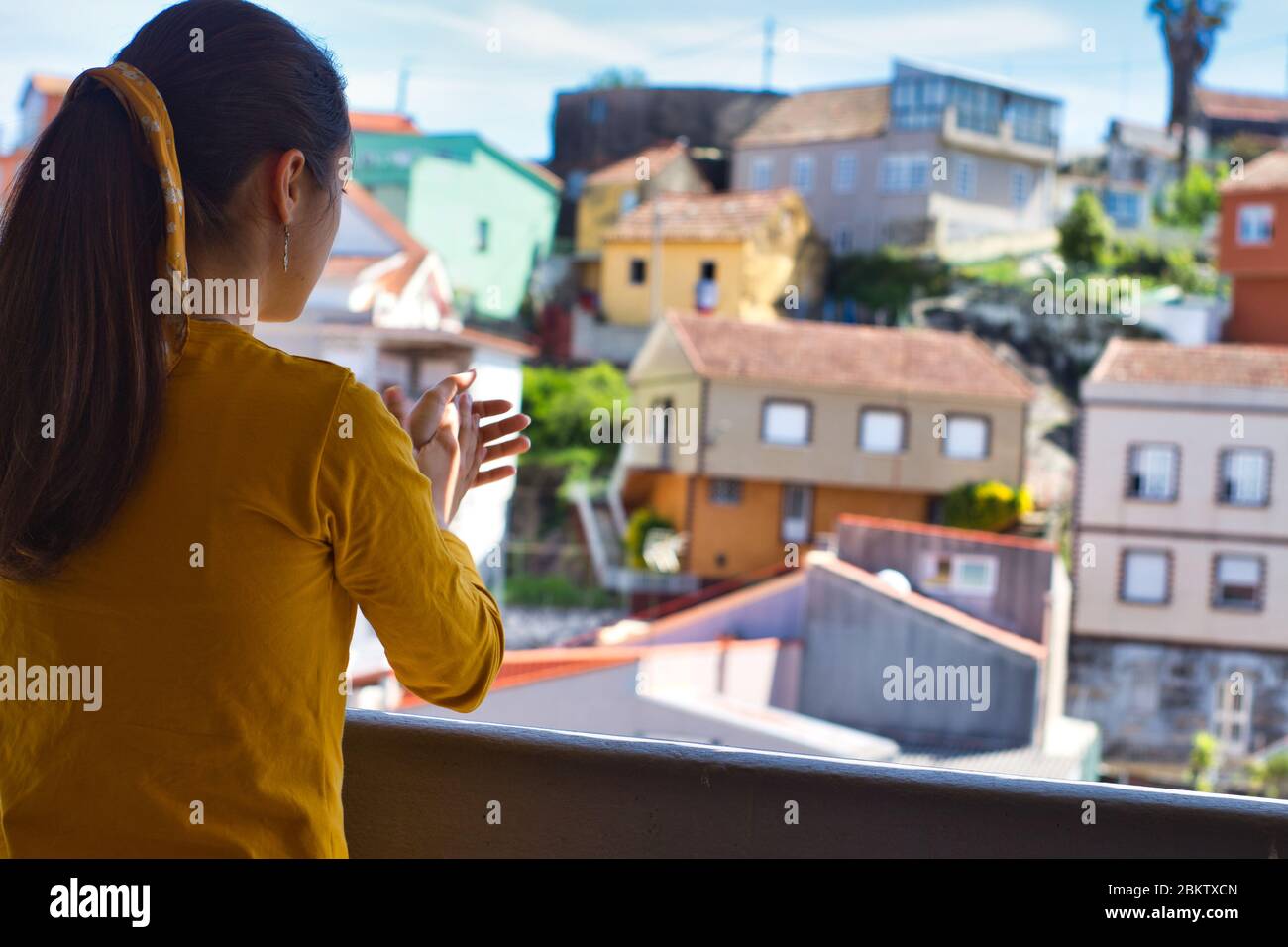 Giovane donna che le ha aggrappato le mani sul balcone per showi gratitudine a tutti gli operatori sanitari durante l'epidemia di coronavirus. Molte case colorate. Foto Stock