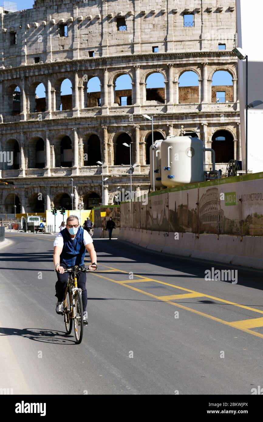 L'uomo che indossa una maschera medica, in bicicletta, passa davanti al Colosseo durante il blocco per Coronavirus Covid 19. Roma, Italia, Europa, UE. Foto Stock
