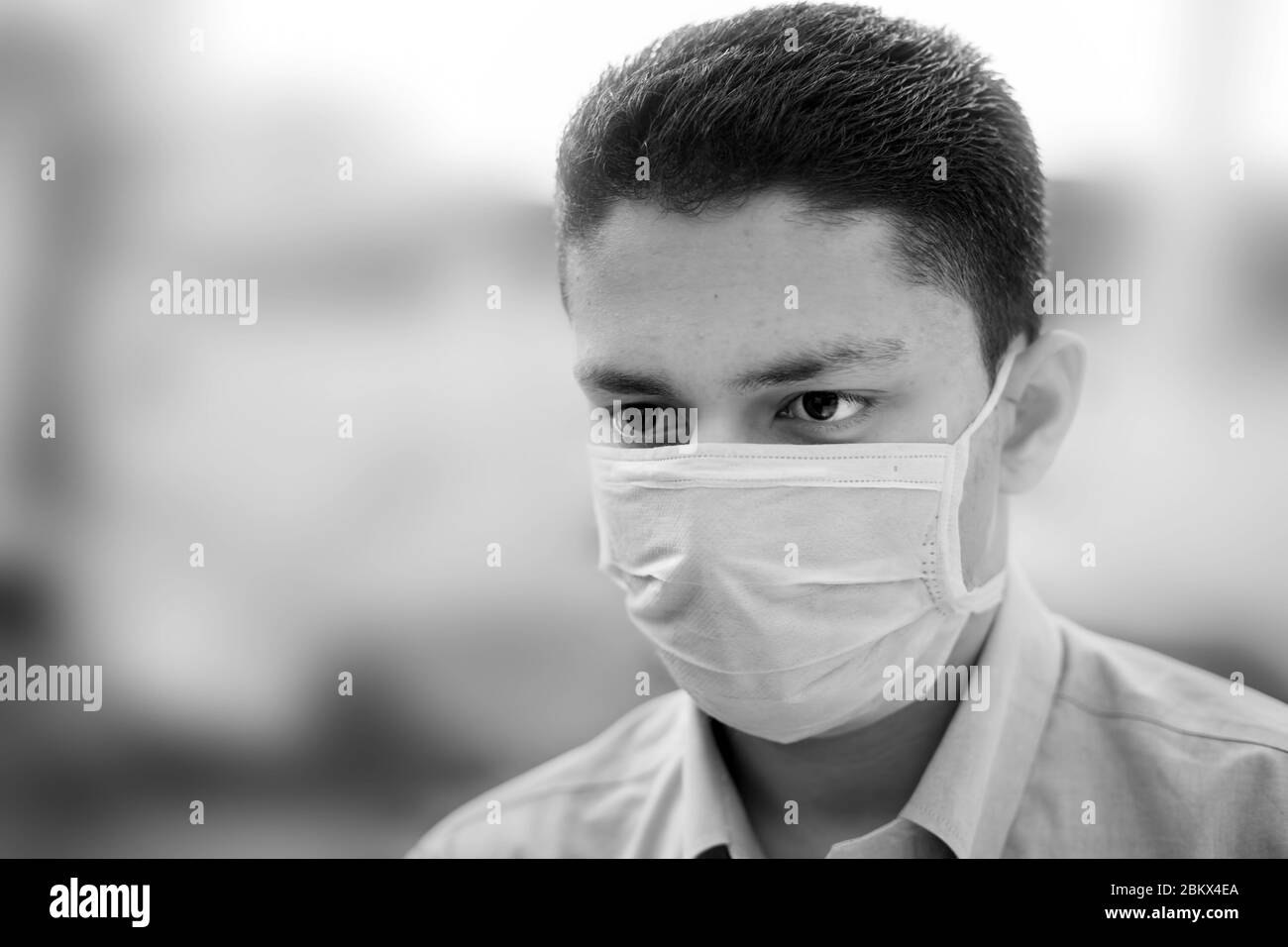 Ritratto di un giovane in camicia di colore blu e con maschera chirurgica o maschera di intervento con sfondo sfocato. Foto Stock