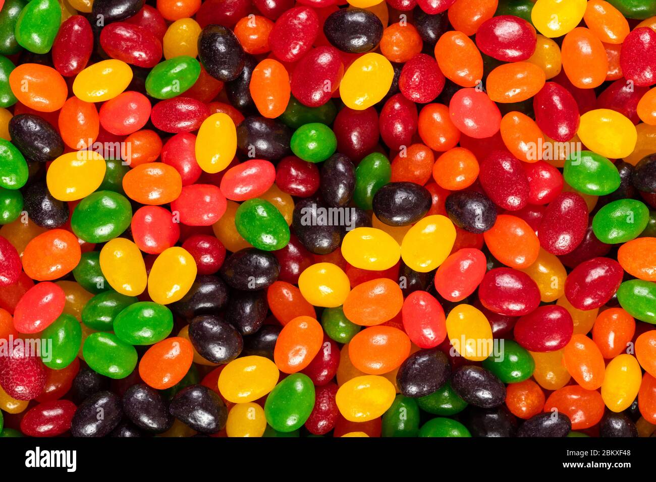 Assortiti colorati fagioli di gelatina nero, rosso, verde, giallo e arancione, dolci sfondo caramella, cibo spazzatura bambini. Foto Stock
