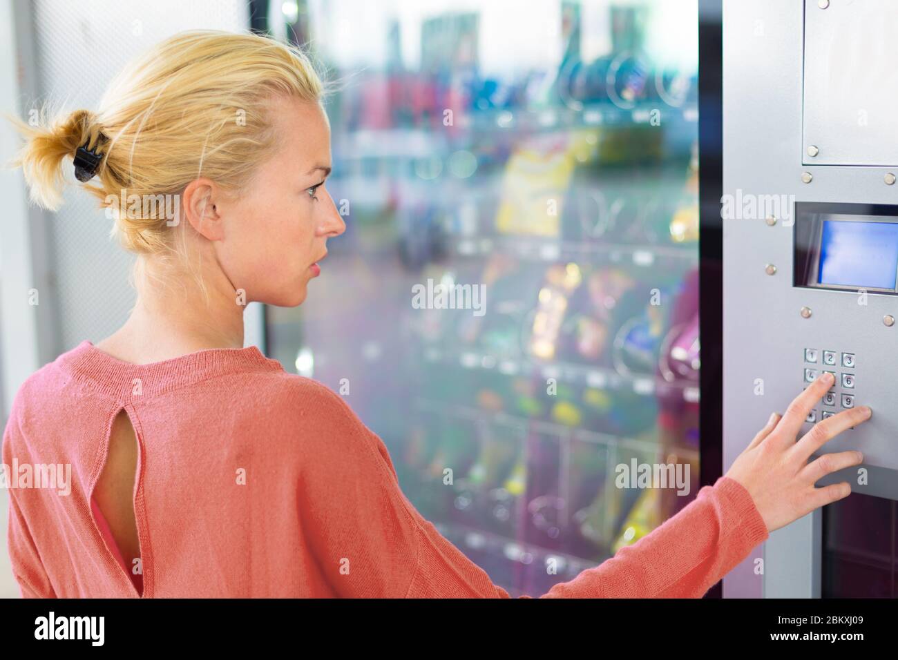 Donna caucasica che usa un distributore automatico moderno. La sua mano destra è posta sul pad del dia Foto Stock