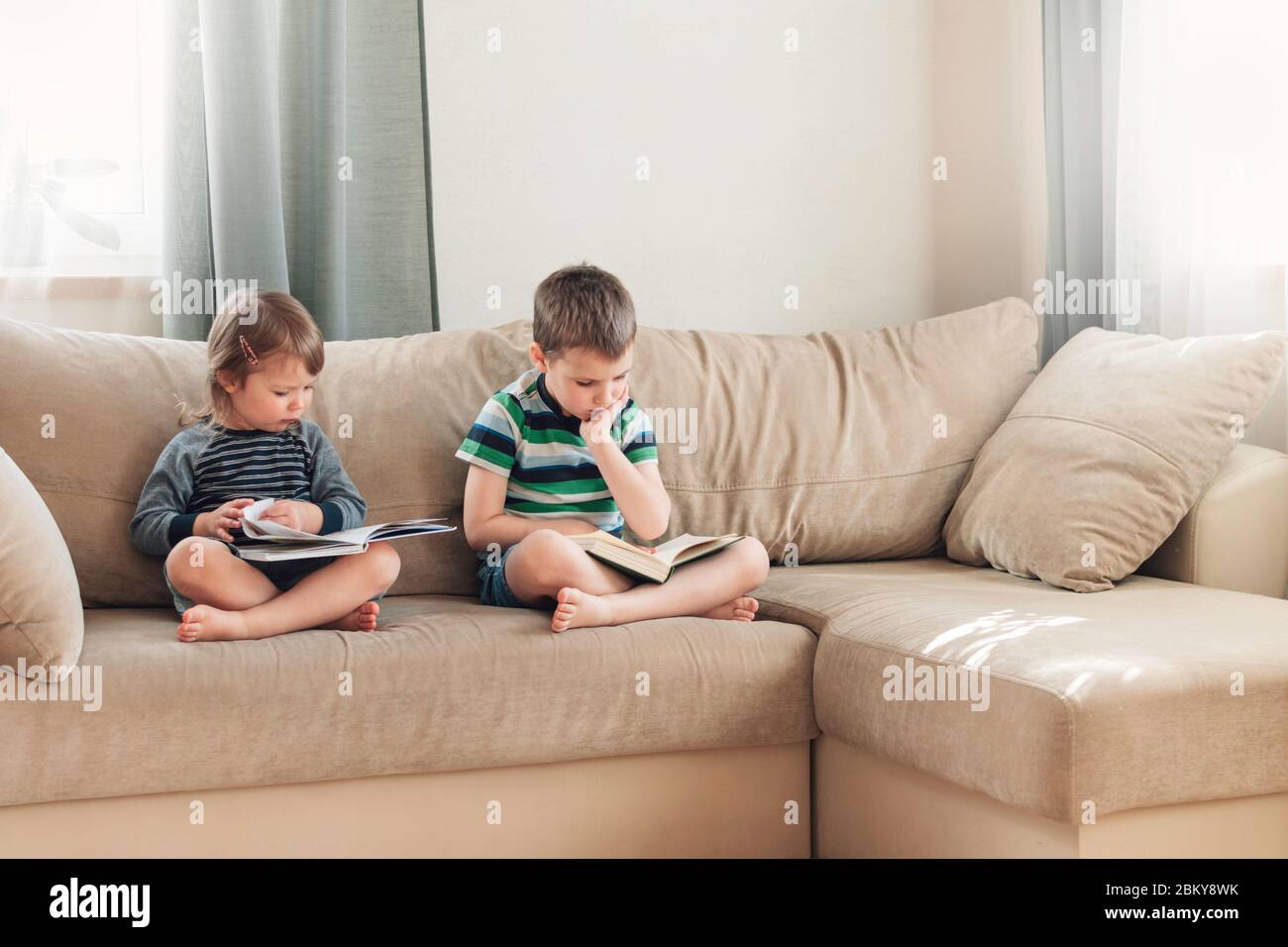 I bambini che leggono un libro a casa sul divano. Formazione a distanza. Detox digitale. Foto Stock