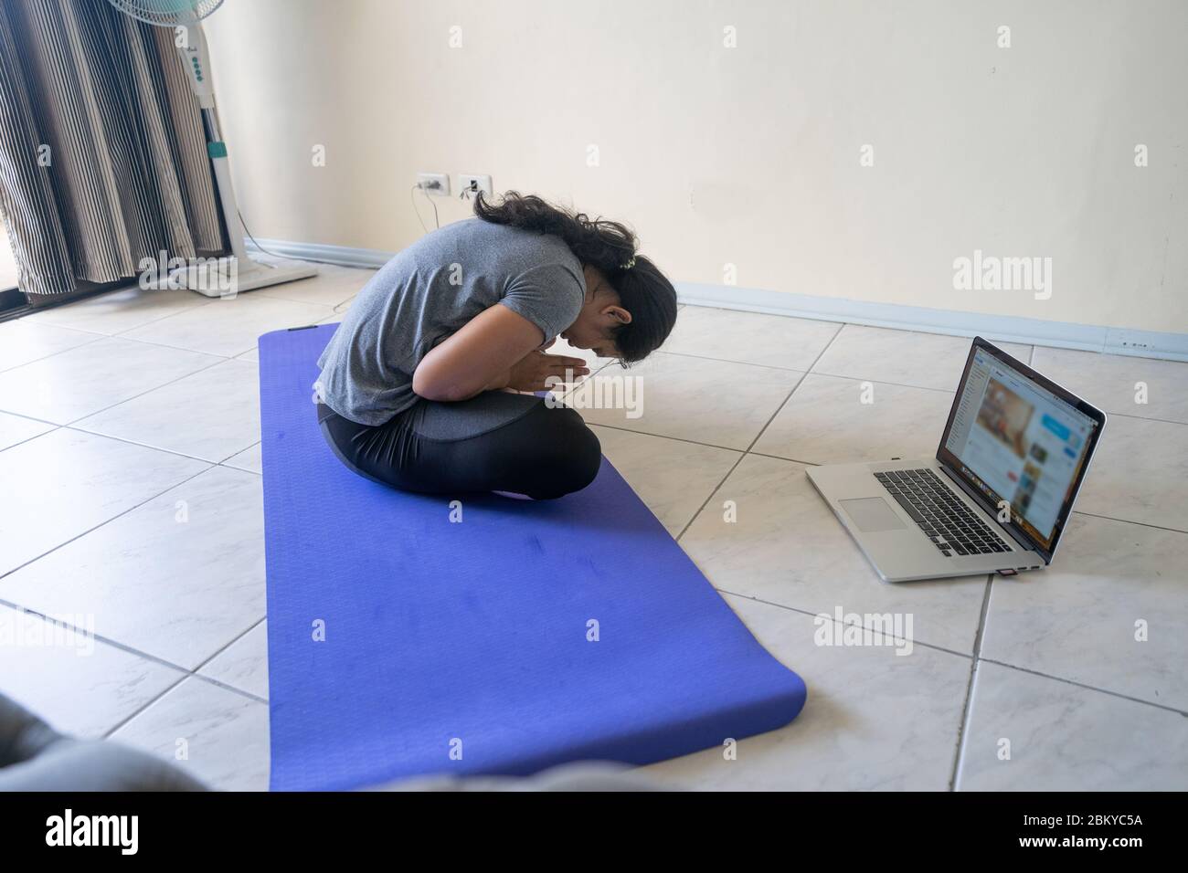 Una donna che intraprendendo una lezione di fitness fisica in linea all'interno di un appartamento durante un periodo di blocco del COVID-19 Pandemic 2020. Foto Stock