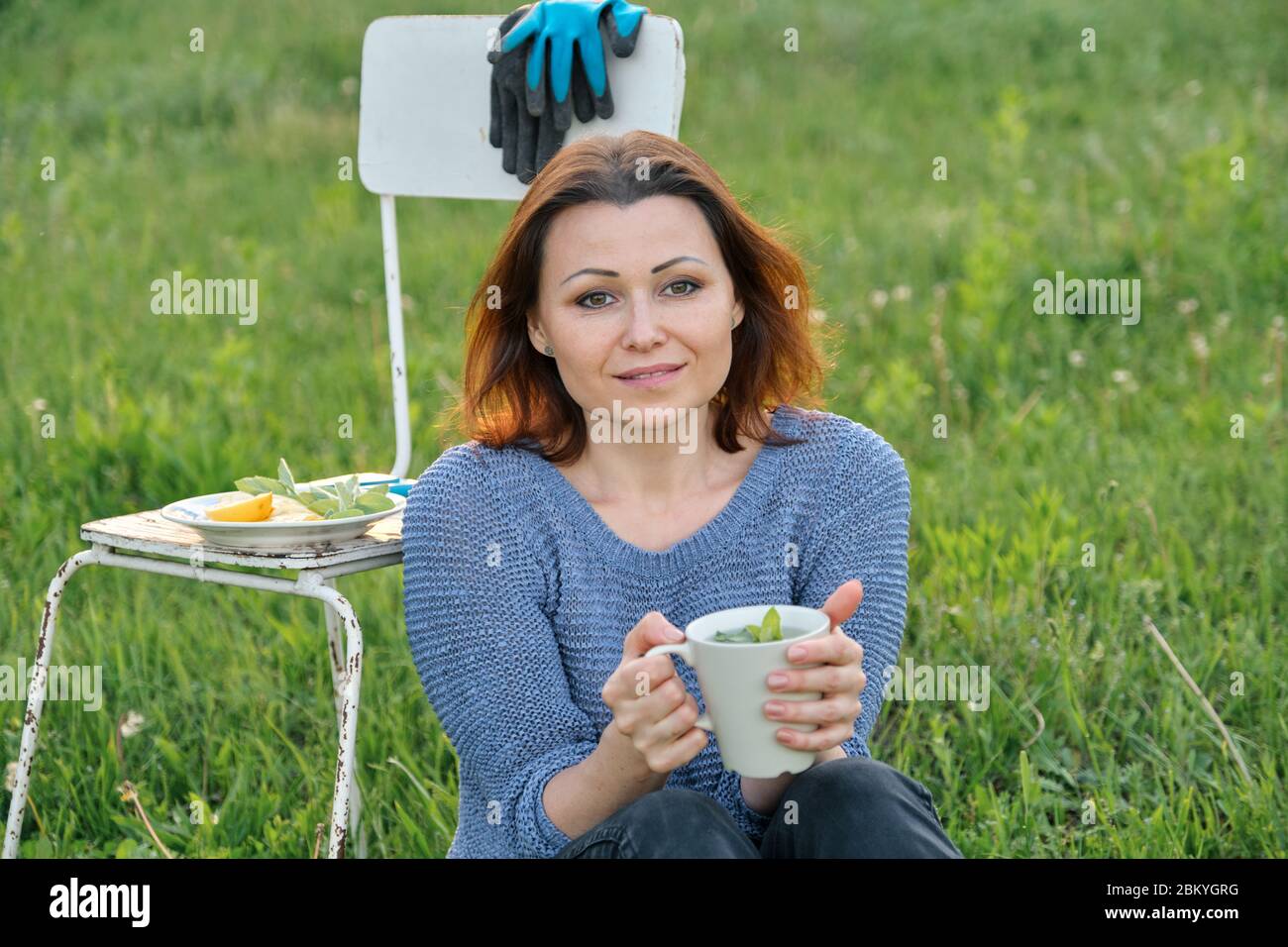 Bella donna di mezza età seduta su erba in giardino, rilassante al tramonto Foto Stock