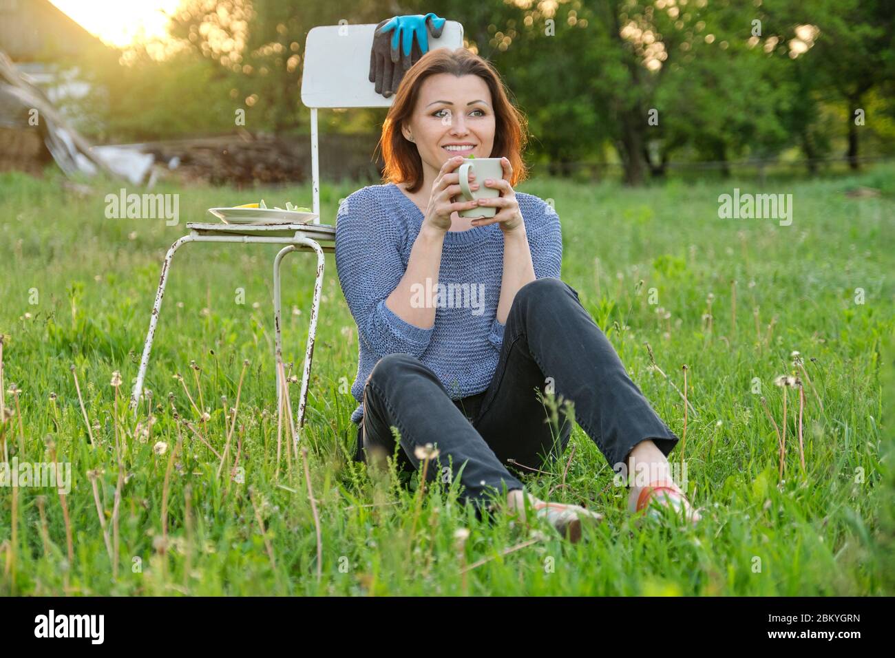 Bella donna di mezza età seduta su erba in giardino, rilassante al tramonto Foto Stock