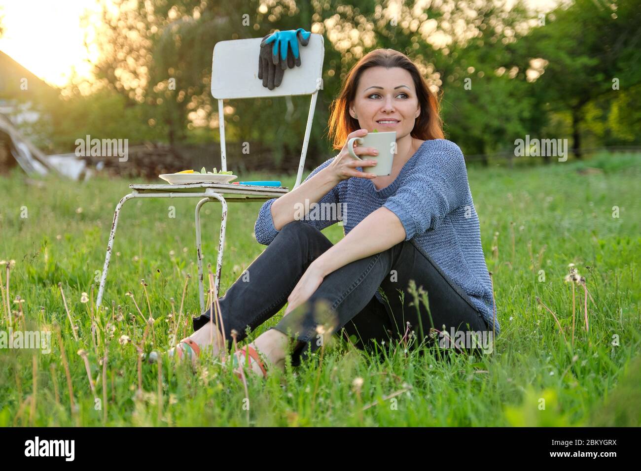 Bella donna di mezza età seduta su erba in giardino, rilassante al tramonto Foto Stock
