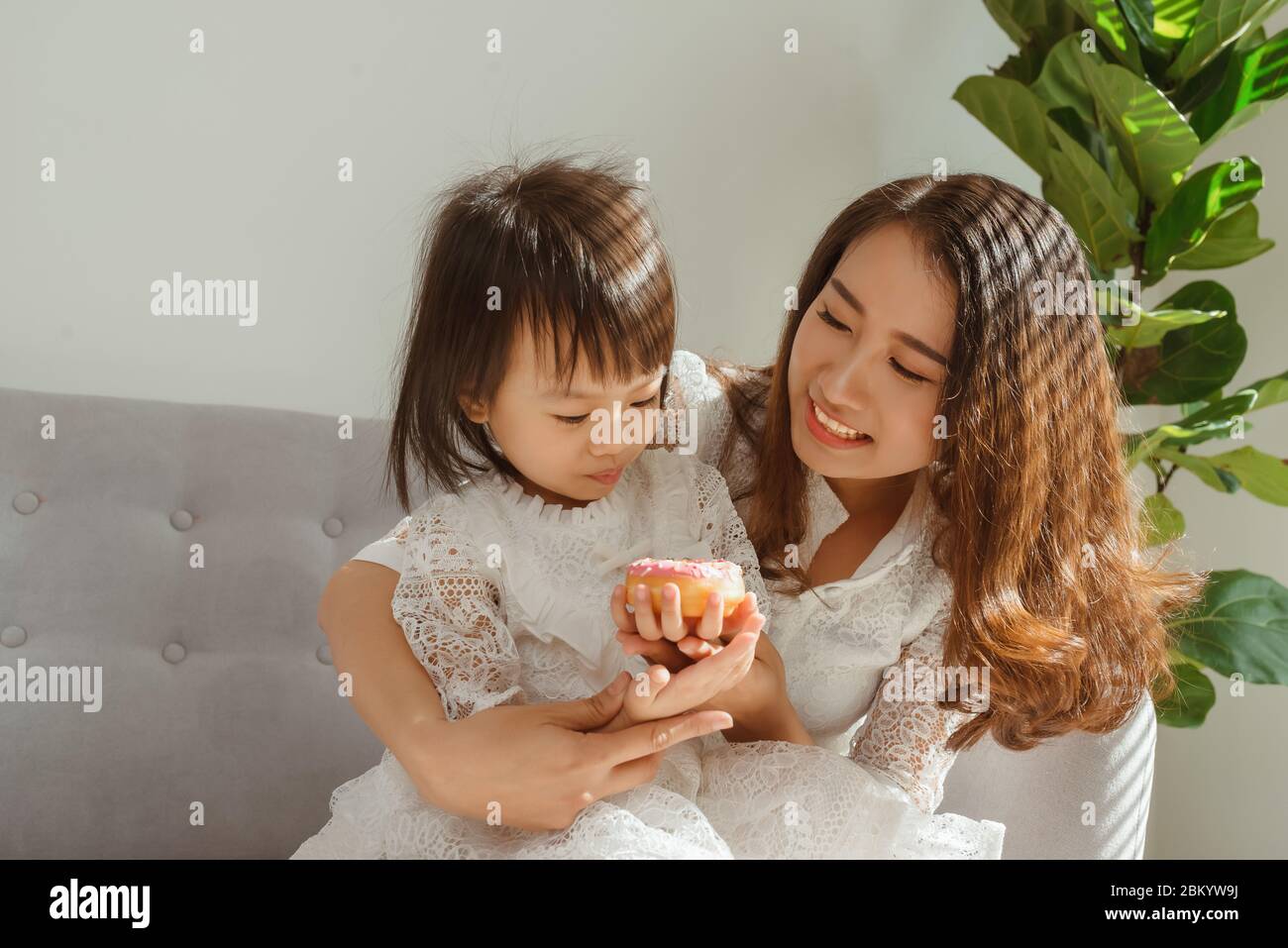 Mamma e figlia di bambini mangiano ciambella quando si siede sul divano a casa Foto Stock