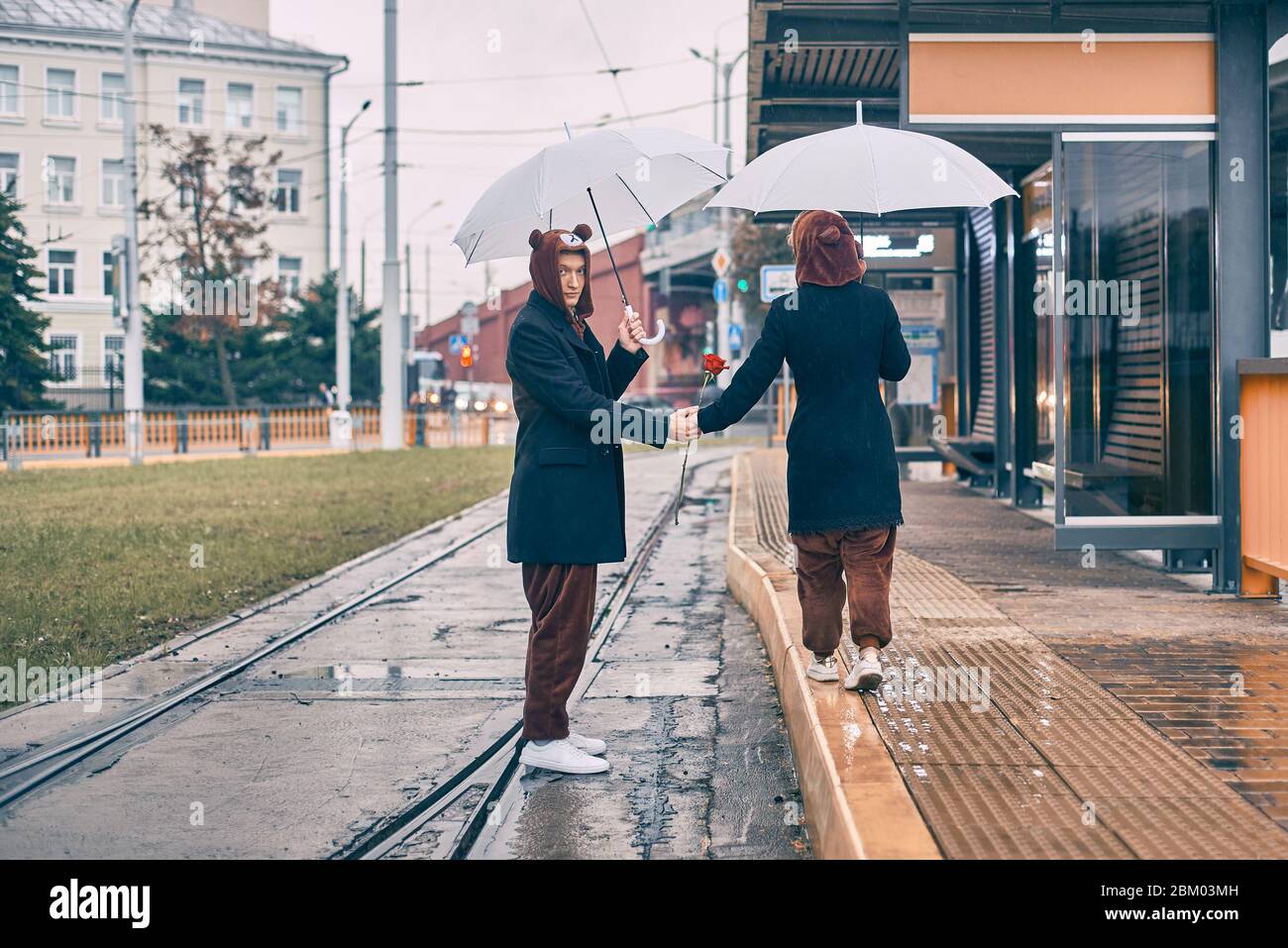 giovane coppia cammina lungo la strada sotto la pioggia, uomo e donna sotto ombrello in costume da orso Foto Stock